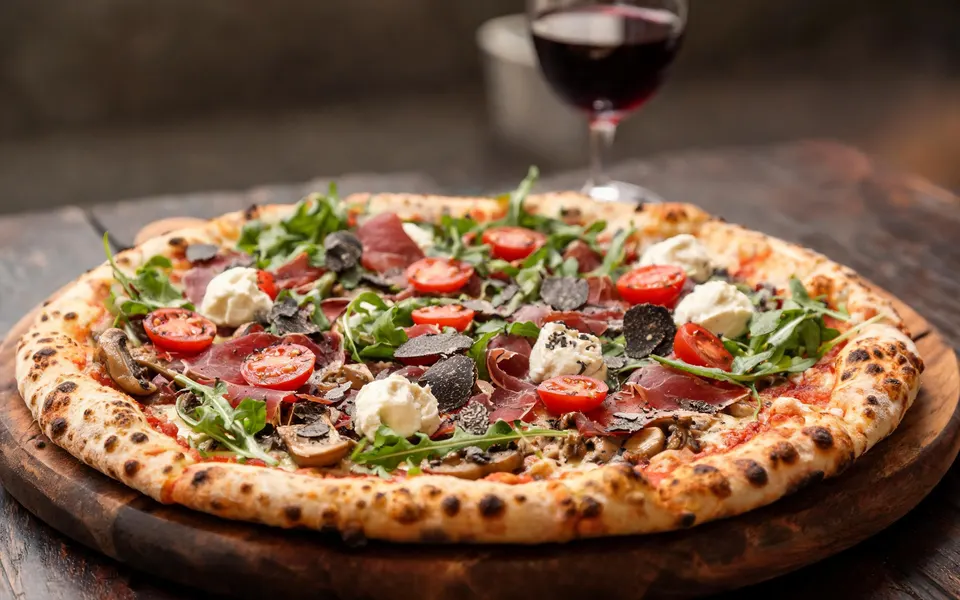 Pizza mit Bresaola, Rucola, Cherrytomaten, Mascarpone und Trüffelhobeln auf einem Holzbrett